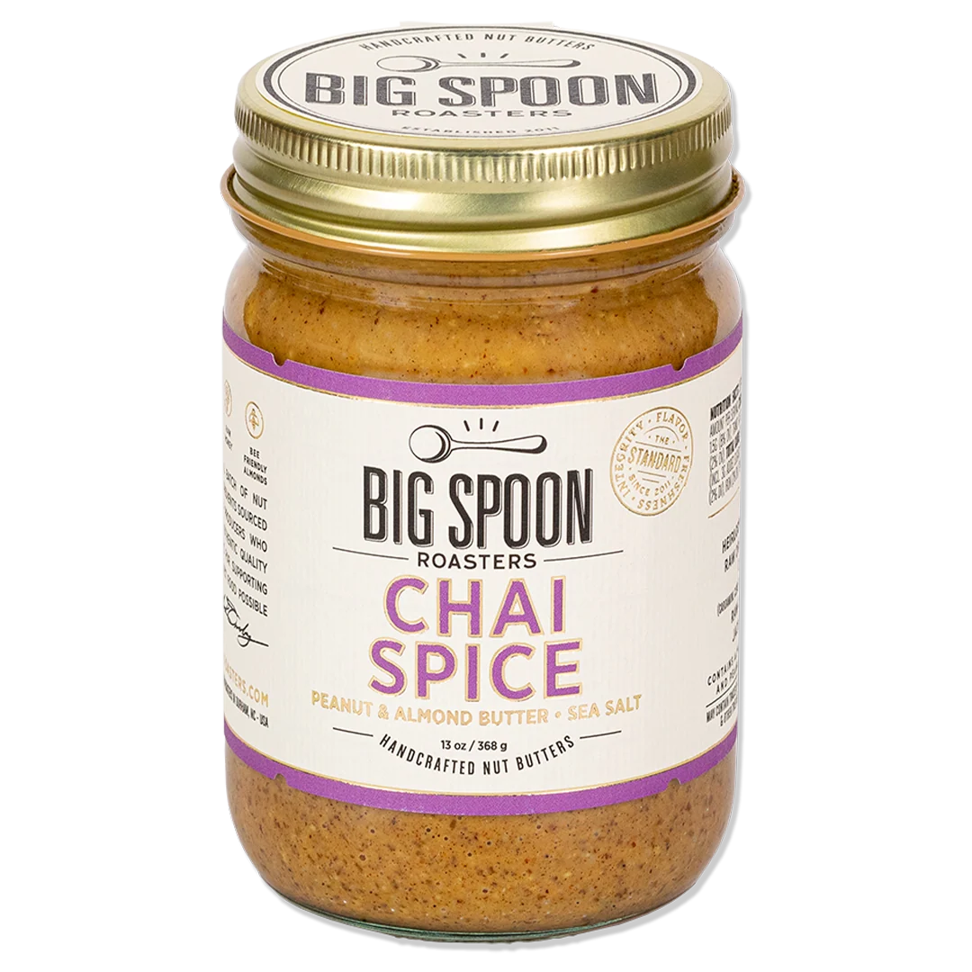 A glass jar of Big Spoon Roasters Chai Spice peanut and almond butter with a gold metal lid and a white label with purple text, set against a plain white background.