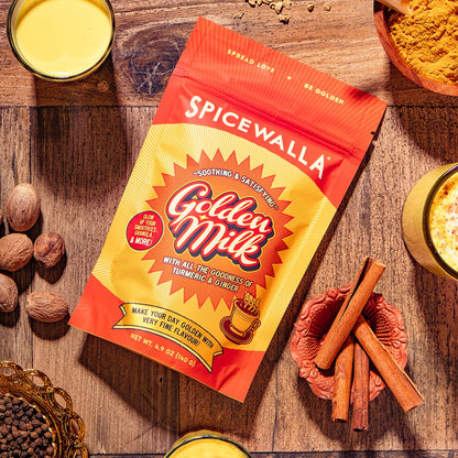 Spicewalla Golden Milk package on a wooden surface with spices and a drink.