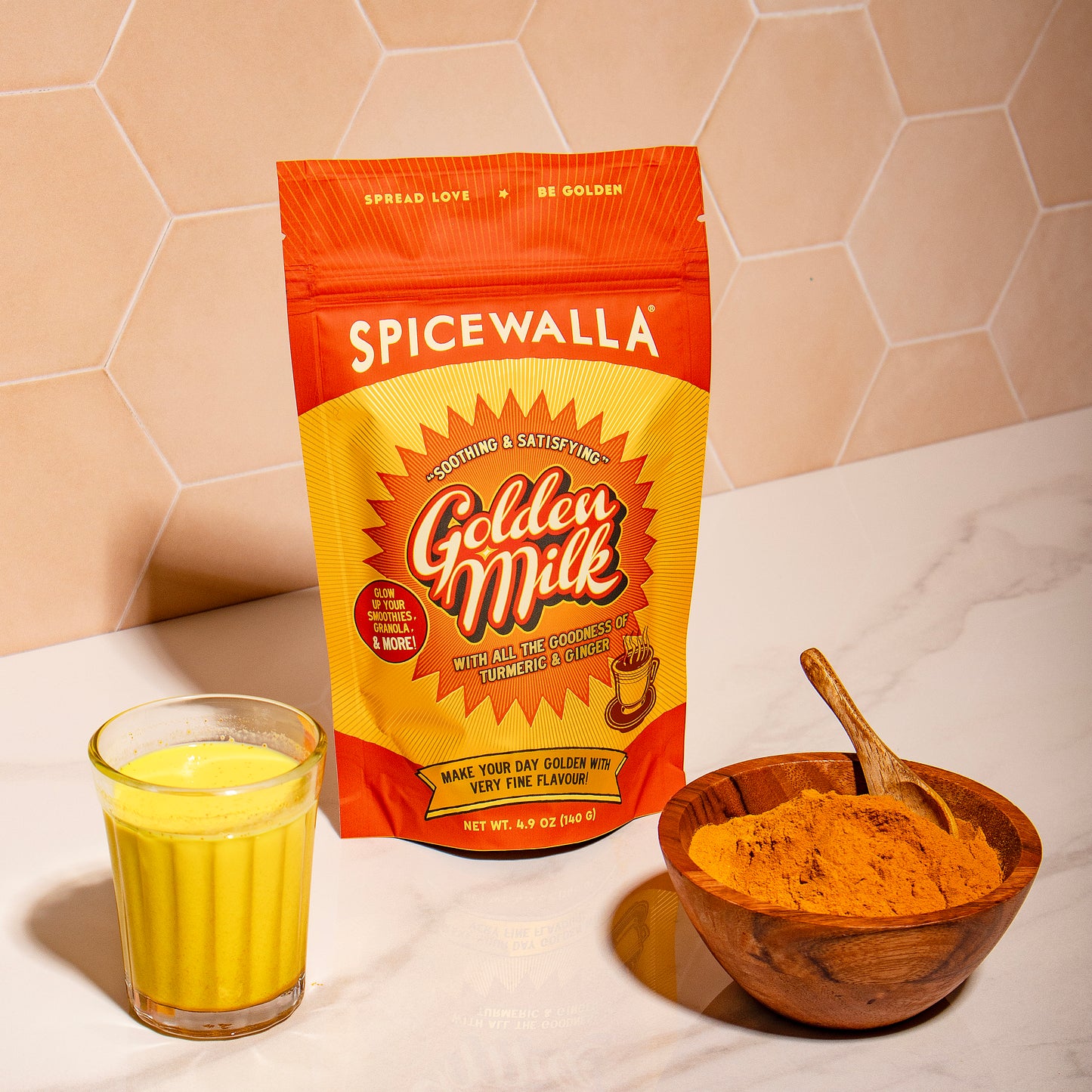 Spicewalla Golden Milk package with a glass of golden milk and a bowl of powder on a marble surface.