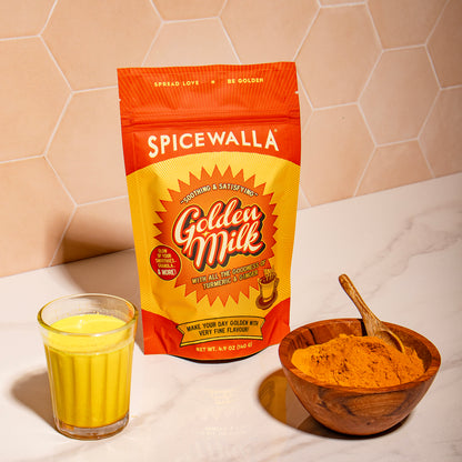 Spicewalla Golden Milk package with a glass of golden milk and a bowl of powder on a marble surface.