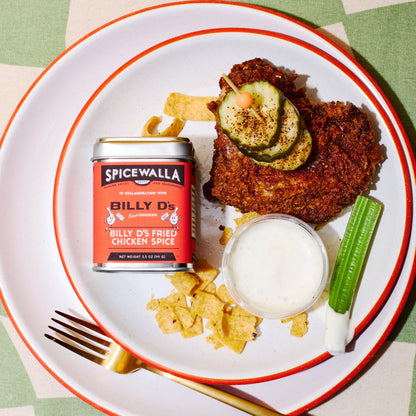 Fried chicken with pickles, chips, and a can of Spicewalla spice on a plate.
