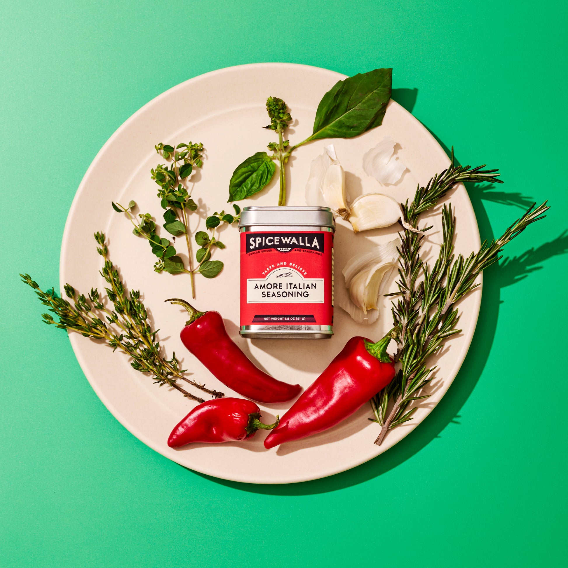 Spicewalla Amore Italian Seasoning tin on a plate with ingredients on a green background