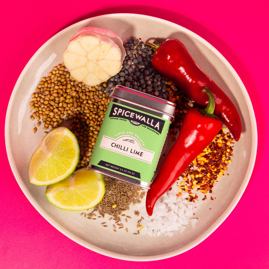Spicewalla Chilli Lime seasoning tin on a plate with spices and herbs against a pink background