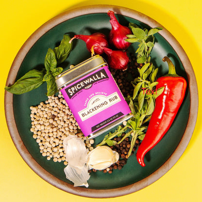 Spicewalla Blackening Rub can surrounded by spices and herbs on a green plate with a yellow background