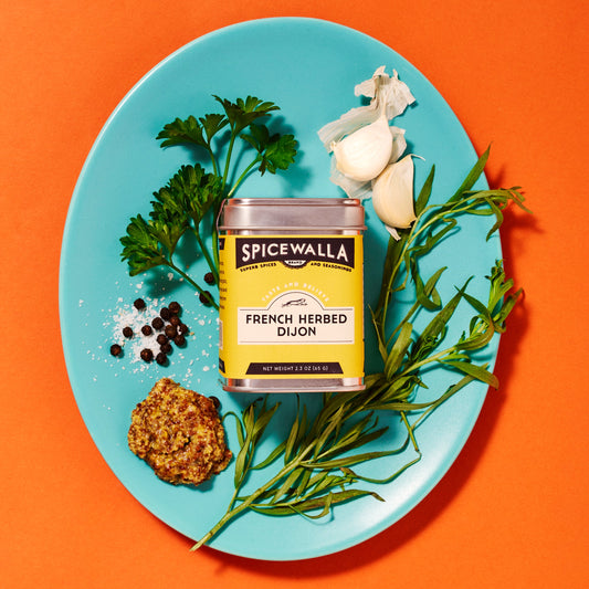 Spicewalla can of French Herbed Onion on a blue plate with herbs and garlic on an orange background