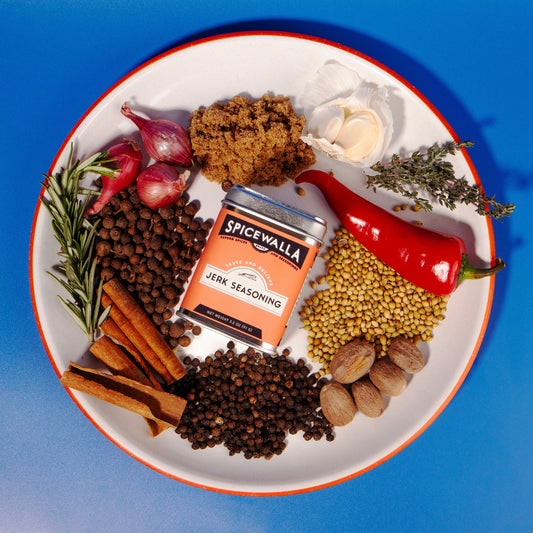 Spicewalla jerk seasoning packet surrounded by various spices on a white plate with a blue background