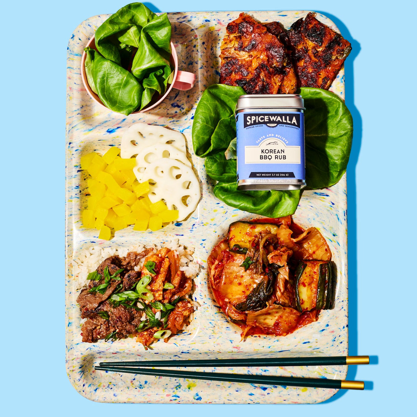 Notebook with food items and a can of Spicewalla Korean BBQ Rub on a blue background