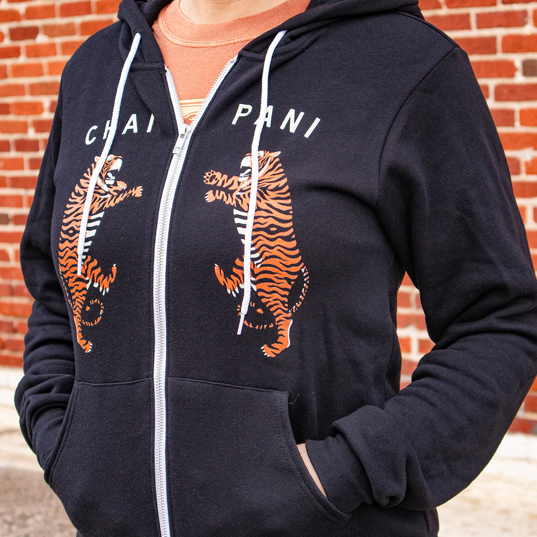 Person wearing a black hoodie with tiger designs in front of a brick wall.