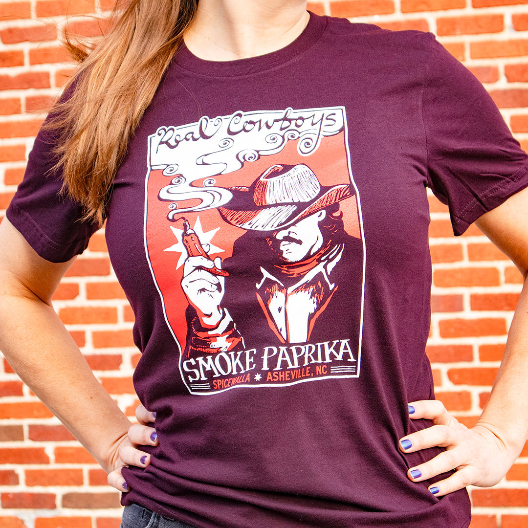 Person wearing a maroon t-shirt with a graphic design in front of a brick wall