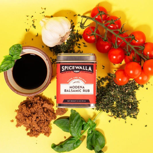 Spicewalla Modena Balsamic Rub can surrounded by tomatoes, herbs, and a bowl of sauce on a yellow background