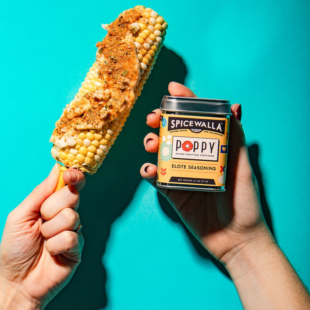 Corn on a stick with Spicewalla Poppy Elote Seasoning against a teal background