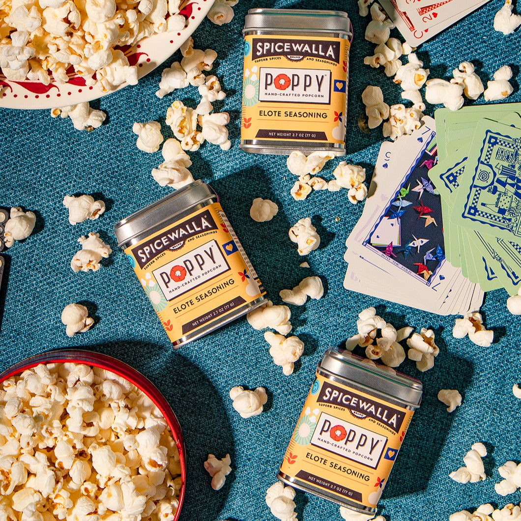 Spicewalla Poppy Elote seasoning tins with popcorn on a blue surface