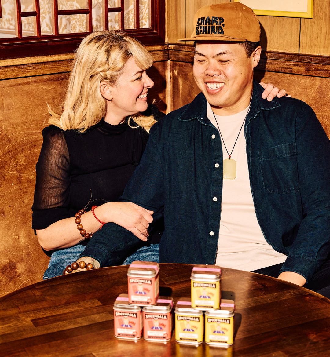 Two people sitting at a wooden table with small boxes in front of them, smiling.