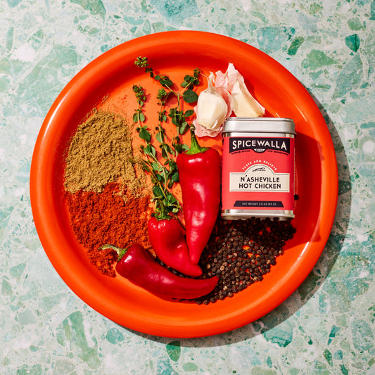 Spice container labeled 'Spicewalla' with red peppers, herbs, and spices on an orange plate.