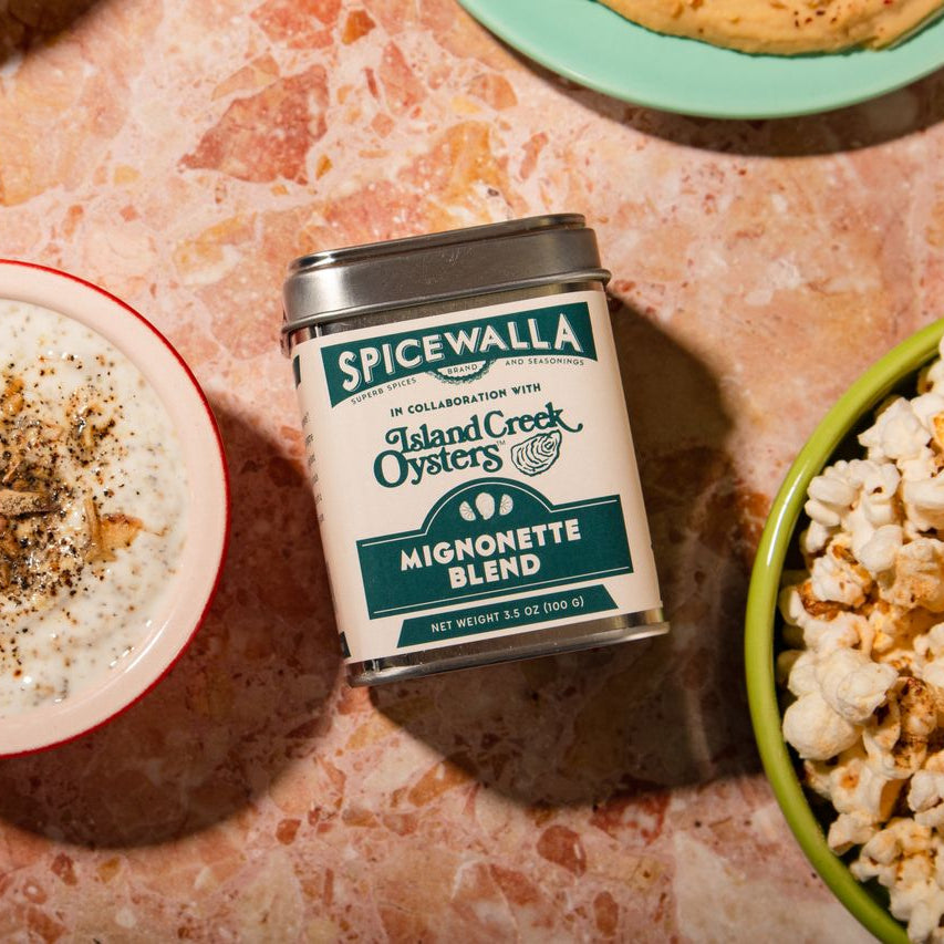 Spicewalla mignonette blend canister on a textured surface with a bowl of popcorn and another dish.