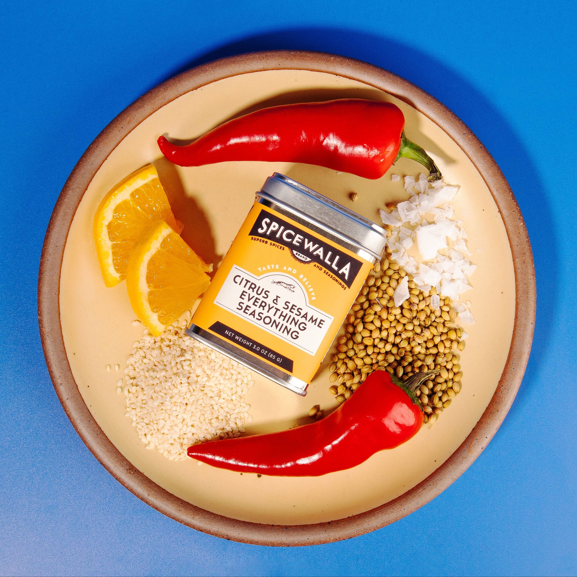 Spicewalla seasoning jar on a plate with spices and herbs against a blue background