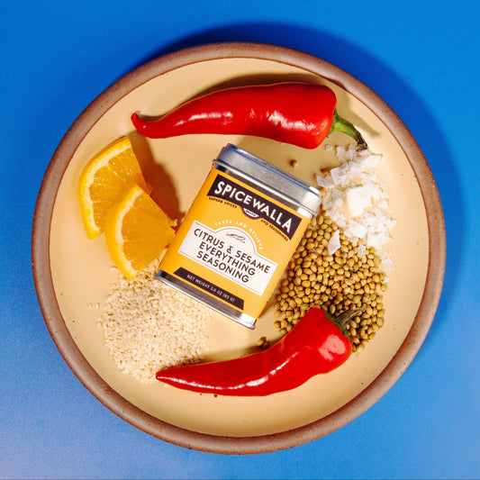 Spicewalla seasoning jar on a plate with spices and herbs against a blue background